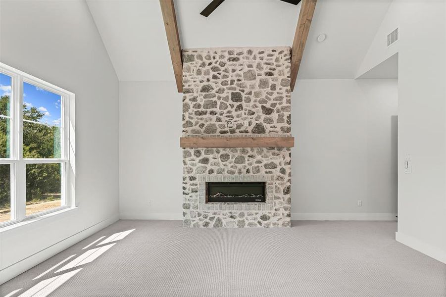 Unfurnished living room featuring carpet, beam ceiling, high vaulted ceiling, a stone fireplace, and a ceiling fan Unfurnished living room featuring carpet, beam ceiling, high vaulted ceiling, a stone fireplace, and a ceiling fan