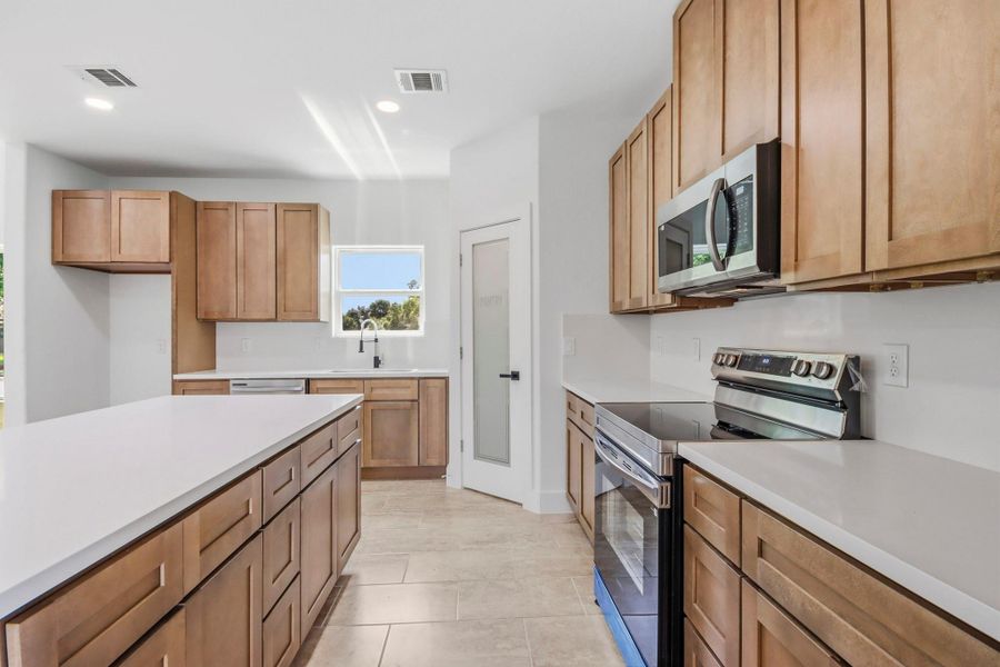 Modern kitchen featuring sleek stainless steel appliances, ample cabinetry, and expansive countertops, all illuminated by natural light from a well-placed window.