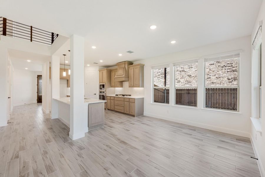 Open-concept living area with kitchen island, tan cabinets, light wood-look floors, and large windows Open-concept living area with kitchen island, tan cabinets, light wood-look floors, and large windows