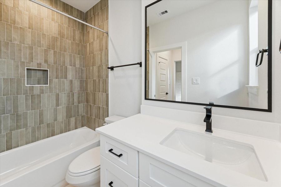 Ensuite bathroom featuring a quartz-topped vanity, matte black fixtures, and a tub-shower combo with warm vertical tile for a modern, spa-inspired finish.