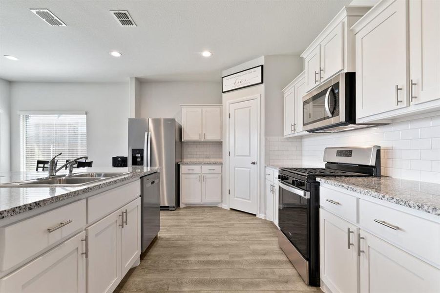 Kitchen featuring appliances with stainless steel finishes, white cabinets, light wood finished floors, decorative backsplash, and light stone counters
