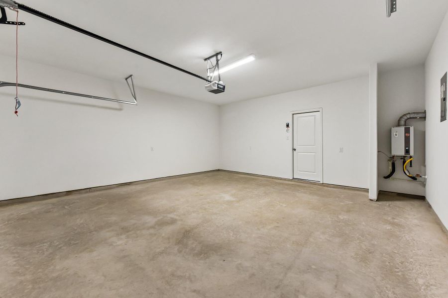 Spacious garage with a concrete floor, painted white walls, overhead lighting, and an automatic garage door opener