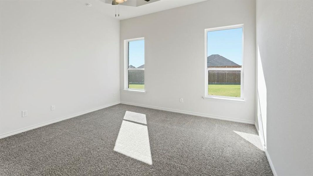 This room features soft gray carpeting, white walls, and two windows providing views of a fenced yard and a distant rooftop This room features soft gray carpeting, white walls, and two windows providing views of a fenced yard and a distant rooftop