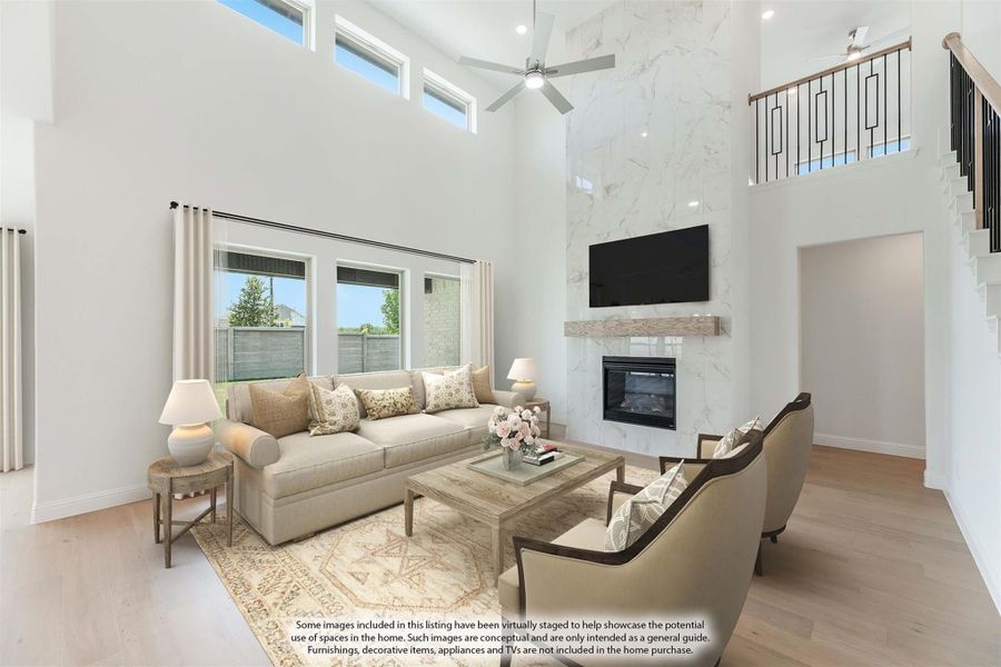 Living room with two-story ceiling, marble fireplace wall, ceiling fan, and hardwood floors