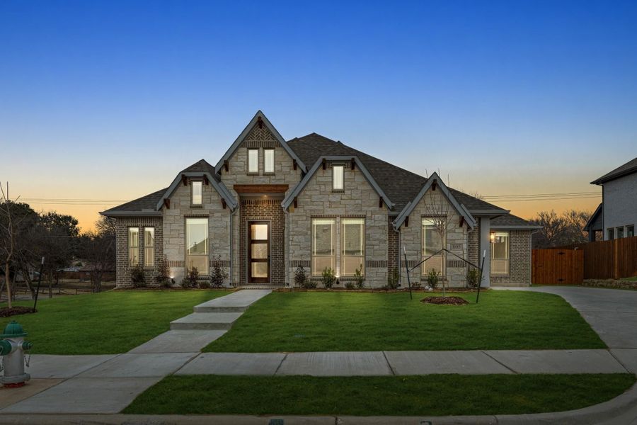 Single-story home with stone and brick exterior, pitched roof, large windows, and green front lawn at dusk Single-story home with stone and brick exterior, pitched roof, large windows, and green front lawn at dusk