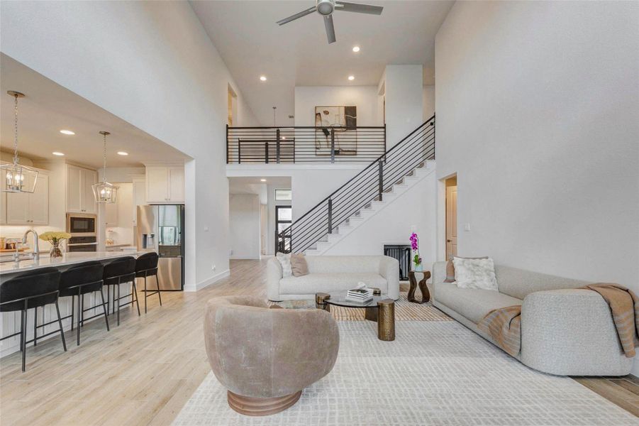 Spacious living area features an open floor plan with high ceilings and a modern design. It includes a sleek kitchen with a large island and bar seating, a comfortable living space , and an upstairs balcony overlooking the main area. Ideal for entertaining and family living. Spacious living area features an open floor plan with high ceilings and a modern design. It includes a sleek kitchen with a large island and bar seating, a comfortable living space , and an upstairs balcony overlooking the main area. Ideal for entertaining and family living.