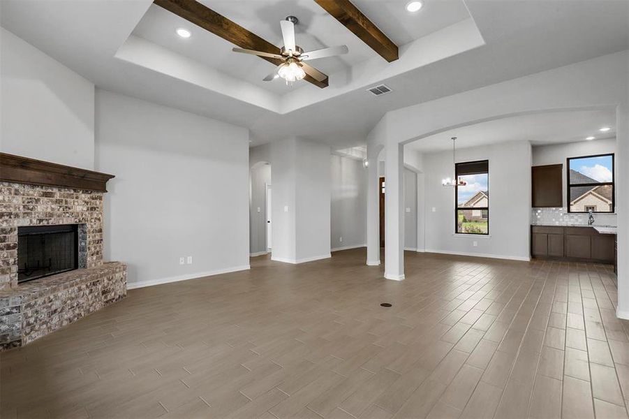 Unfurnished living room with a fireplace, beam ceiling, ceiling fan with notable chandelier, and a raised ceiling