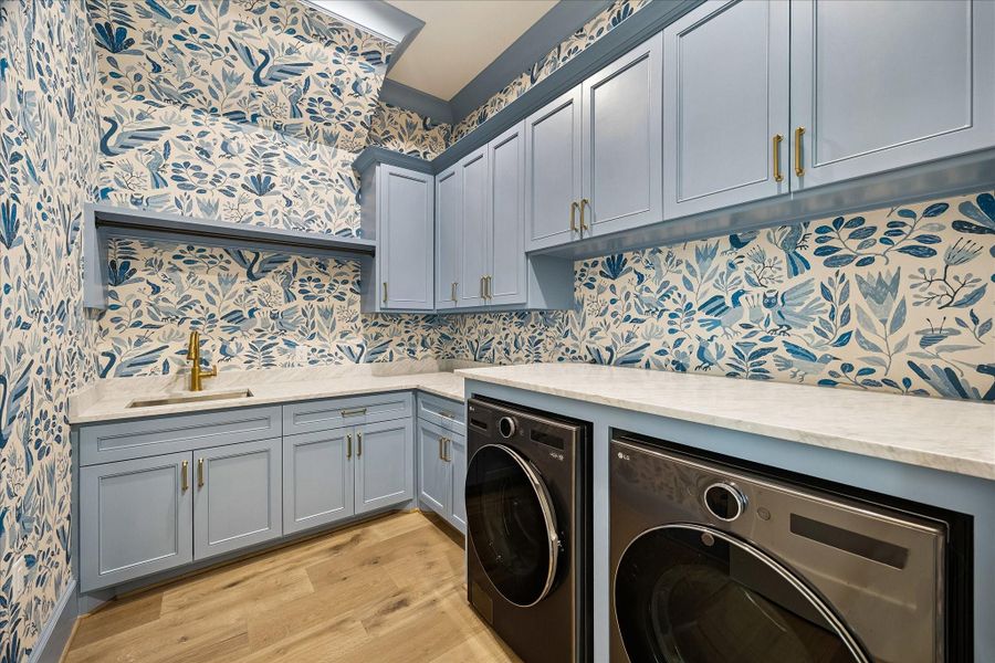The wonderful, happy utility room blends function and design with painted custom cabinetry, honed marble slab countertops, and a deep undermount sink with beautiful hardware. Striking wallpaper to the ceiling, adds a bold, touch with lots of personality, while built-in cabinetry, hanging rod, and space for a full-size washer and dryer with folding space create a highly functional and stylish workspace.