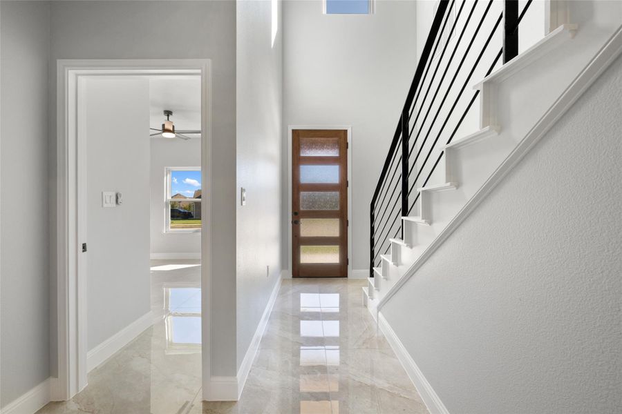 Entrance foyer featuring light marble finish floors, a ceiling fan, stairway, and a high ceiling