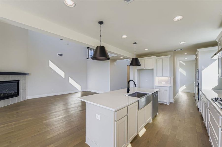Kitchen featuring a center island with sink, pendant lighting, open floor plan, dark wood-style floors, and a tiled fireplace