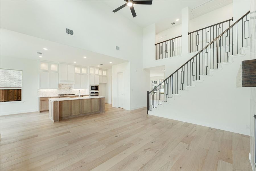 Open-concept living area with kitchen island, white cabinets, hardwood floors, and staircase with iron railings