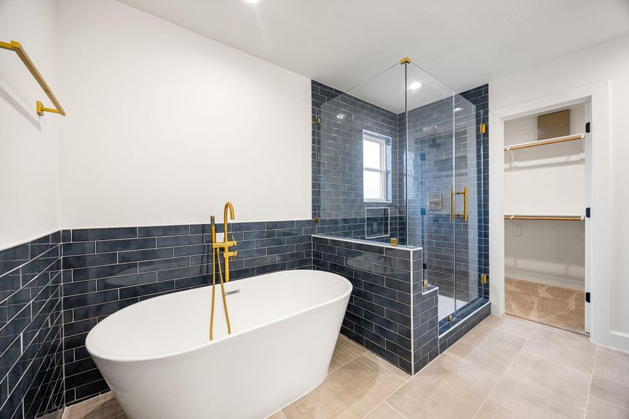 Stunning primary bathroom featuring a freestanding soaking tub with gold fixtures and a glass-enclosed walk-in shower. Beautiful blue tile surrounds add character and contrast, creating a spa-inspired retreat with a modern, upscale feel.