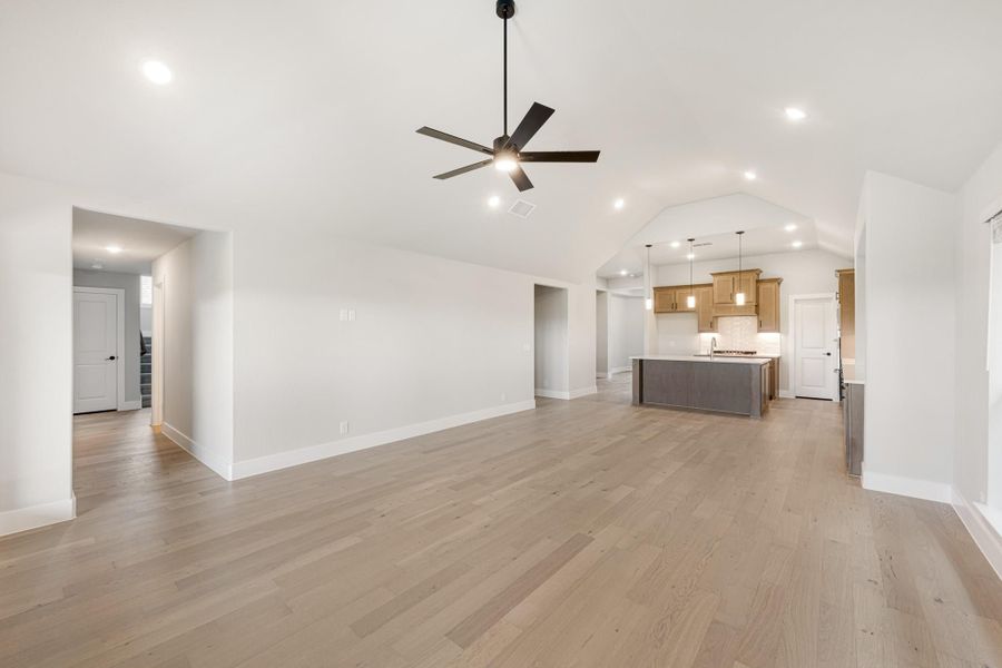 Open living area with hardwood floors, vaulted ceiling, ceiling fan, and open-concept kitchen with island in background. Open living area with hardwood floors, vaulted ceiling, ceiling fan, and open-concept kitchen with island in background.