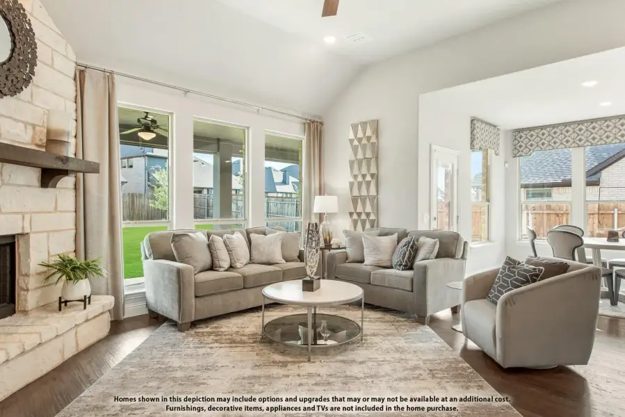 Living room with stone fireplace, vaulted ceiling, gray sofas, and hardwood floors with large backyard-facing windows