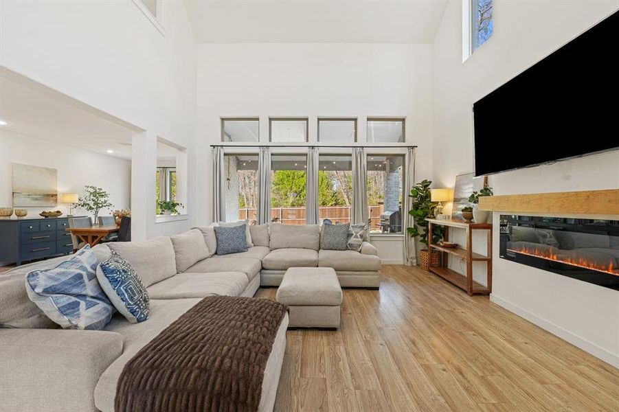 Living area featuring a high ceiling, healthy amount of natural light, light wood-style floors, and a glass covered fireplace