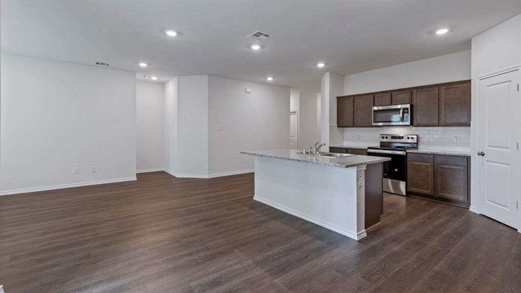 Kitchen with stainless steel appliances, dark wood finish cabinetry, a center island with sink, dark wood-style flooring, and recessed lighting