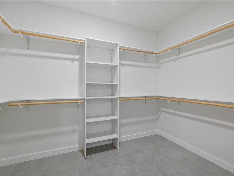 The property features a spacious walk-in closet with extensive built-in shelving, hanging rods, and a central shelving unit, all set against white walls and a gray tiled floor