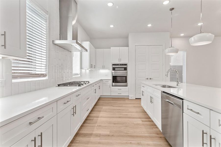 Kitchen with decorative light fixtures, wall chimney range hood, white cabinets, appliances with stainless steel finishes, and recessed lighting