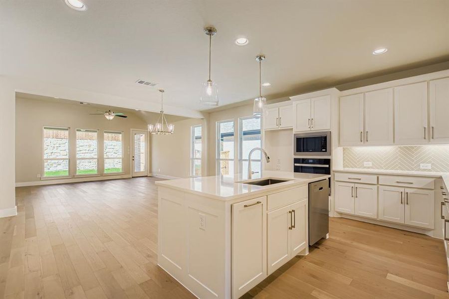 Kitchen with tasteful backsplash, an island with sink, recessed lighting, a chandelier, and pendant lighting