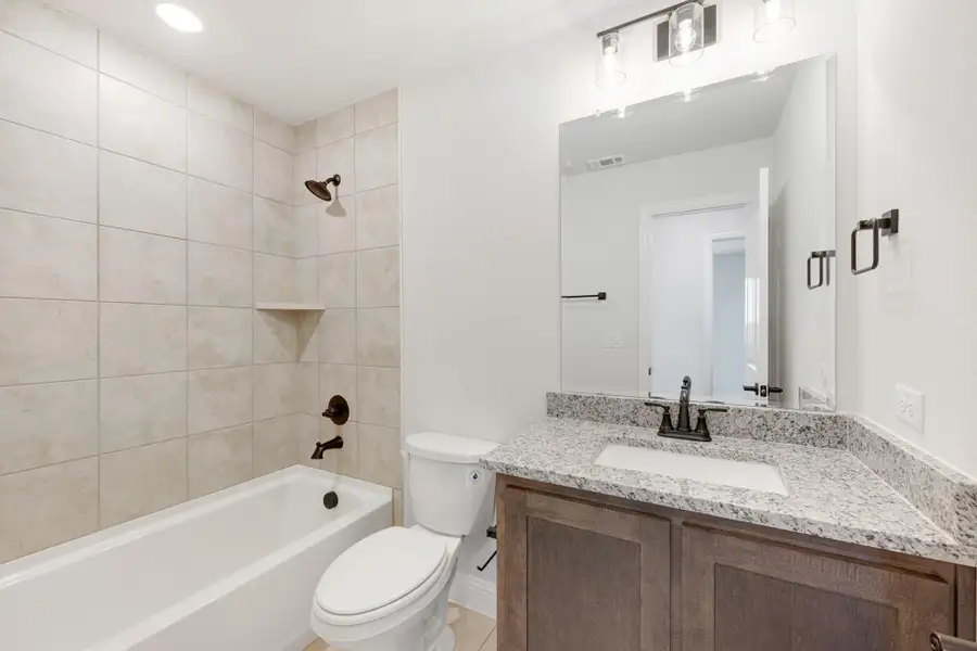Bathroom with tiled tub-shower combo, wood vanity with granite countertop, and large mirror Bathroom with tiled tub-shower combo, wood vanity with granite countertop, and large mirror