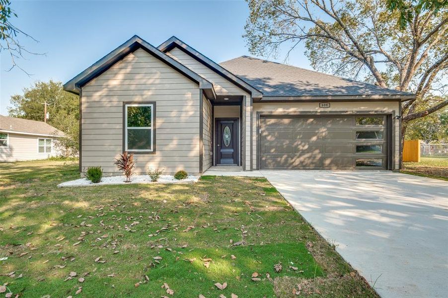 View of front of property featuring concrete driveway, a front lawn, a garage, and roof with shingles