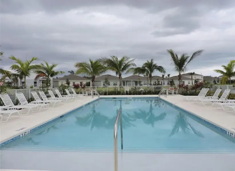 Rectangular swimming pool featuring a tiled waterline, built-in entry steps, a metal handrail, and a surrounding concrete deck enclosed by a perimeter fence