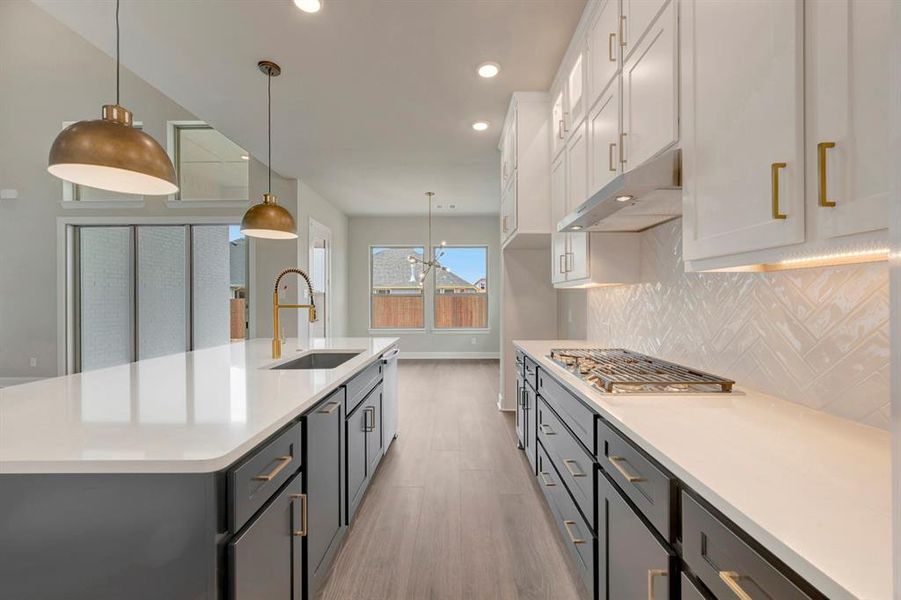 Kitchen featuring hanging light fixtures, light wood finished floors, light stone counters, a center island with sink, and dual tone cabinetry