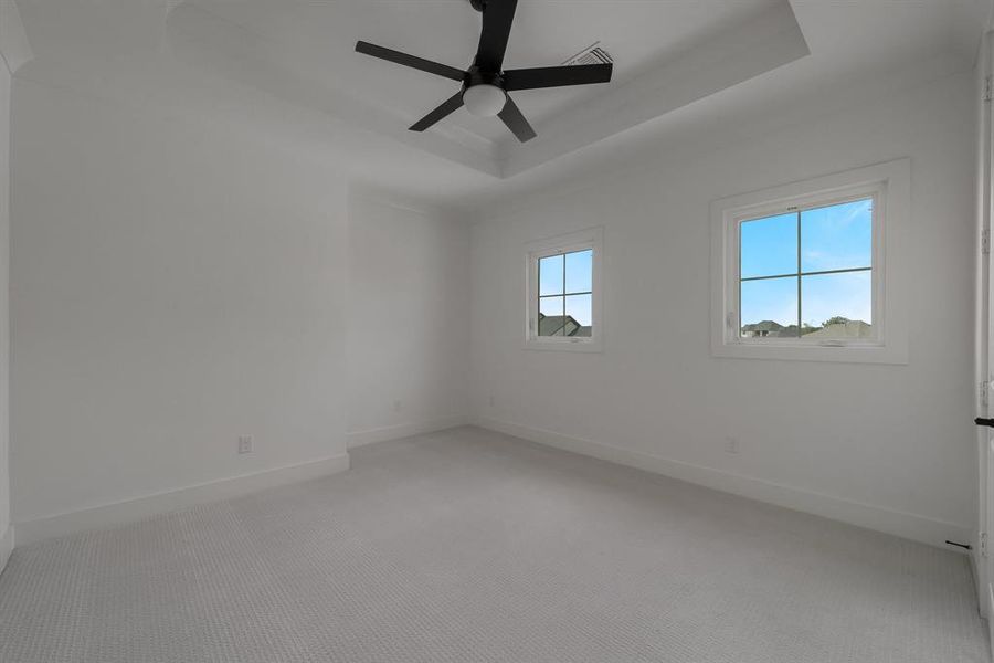 Empty room featuring ceiling fan, a tray ceiling, and light colored carpet