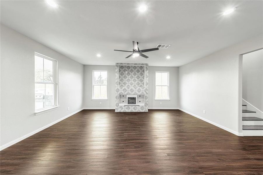 Unfurnished living room with dark wood-type flooring, ceiling fan, recessed lighting, healthy amount of natural light, and a tiled fireplace
