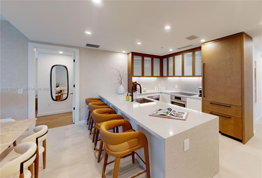 Kitchen featuring an expansive stone-topped island with integrated seating, wood-finish cabinetry, frosted glass cabinet doors, recessed lighting, and a gooseneck faucet. Images are for finish purposes only. Please refer to the floor plan for the layout. Kitchen featuring an expansive stone-topped island with integrated seating, wood-finish cabinetry, frosted glass cabinet doors, recessed lighting, and a gooseneck faucet. Images are for finish purposes only. Please refer to the floor plan for the layout.