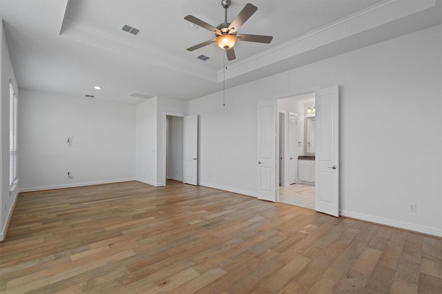 Spacious room featuring wood-finish flooring, a tray ceiling, and a ceiling fan with integrated lighting