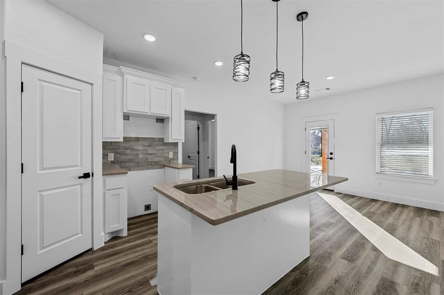 Kitchen featuring tasteful backsplash, sink, decorative light fixtures, white cabinetry, and an island with sink