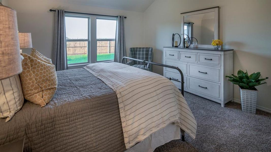 Carpeted bedroom featuring a double window with a backyard view, vaulted ceiling, and a white dresser with a dark countertop and framed mirror