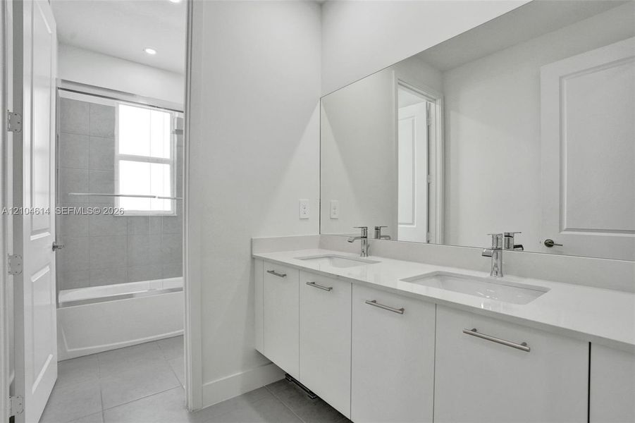Dual vanity with chrome fixtures and ample counter space, full-width mirror, recessed lighting, and a bathtub with a sliding glass enclosure
