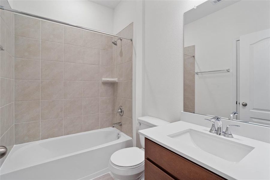 Secondary bathroom features stained cabinets, neutral paint, shower/tub combo with tile surround, large mirror, tile floors, and sleek fixtures and modern finishes.