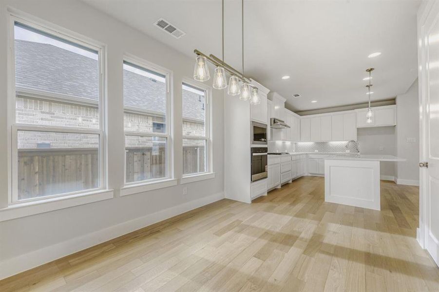 Kitchen with white cabinets, hanging light fixtures, light wood-style floors, a kitchen island, and backsplash