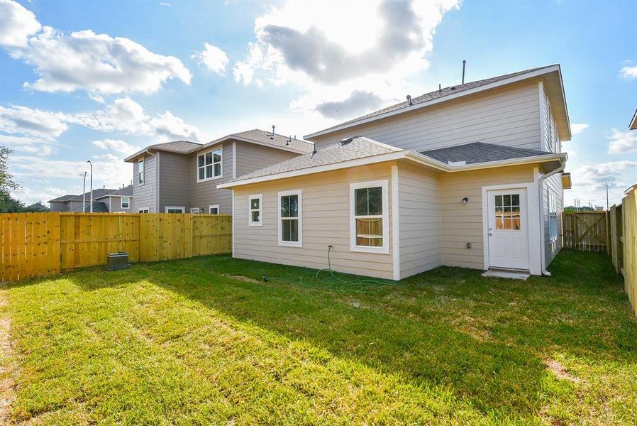 Backyard of a modern two-story house with a wooden fence, green lawn, and a clear sky.