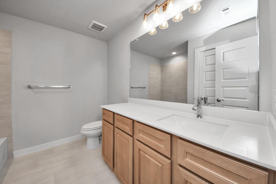 Secondary bath features tile flooring, walk-in shower with tile surround, light stained wood cabinets, beautiful light countertop.