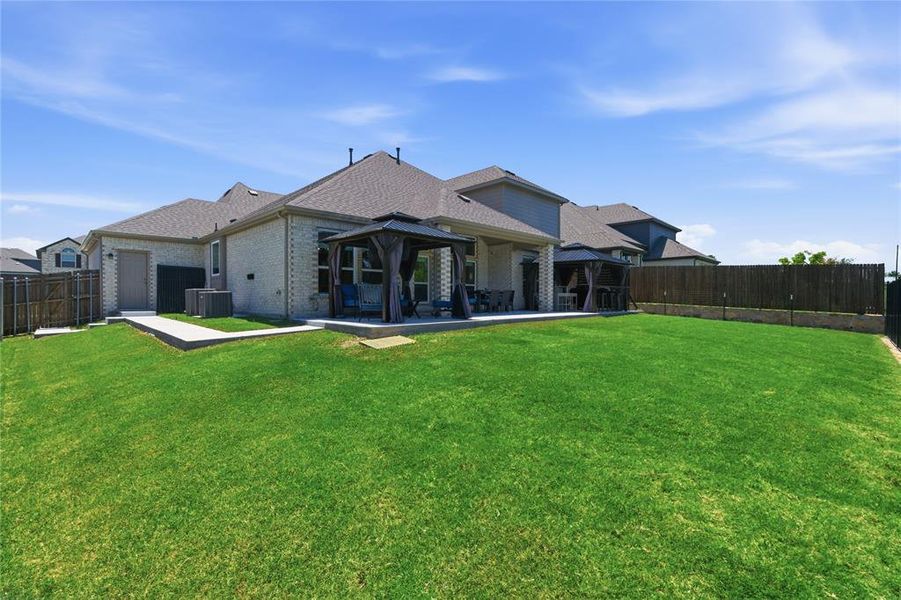 Spacious backyard featuring an expansive lawn, a covered patio with an outdoor gazebo, and a privacy fence