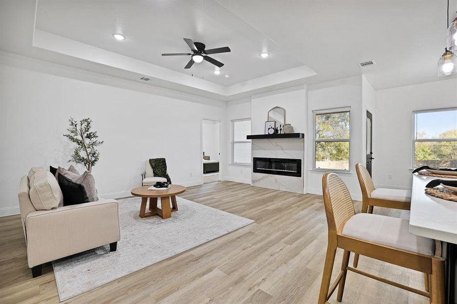 Living room with a high end fireplace, a tray ceiling, and light hardwood / wood-style flooring