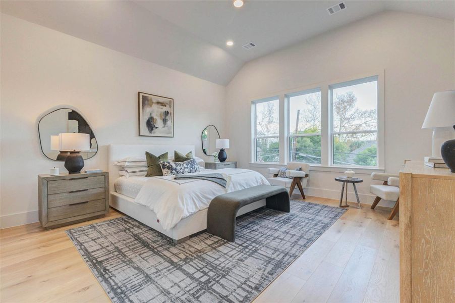 Spacious primary retreat with high, angled ceilings and three large windows allowing abundant natural light. The light wood floors and neutral walls create a bright and airy ambiance ideal for personalization.