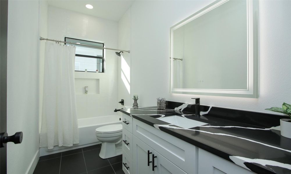 This bathroom features a modern design quartz countertop, white cabinetry, and a large illuminated mirror. It includes a bathtub with a shower combination, white tiles, and a black-framed window for natural light. This bathroom features a modern design quartz countertop, white cabinetry, and a large illuminated mirror. It includes a bathtub with a shower combination, white tiles, and a black-framed window for natural light.