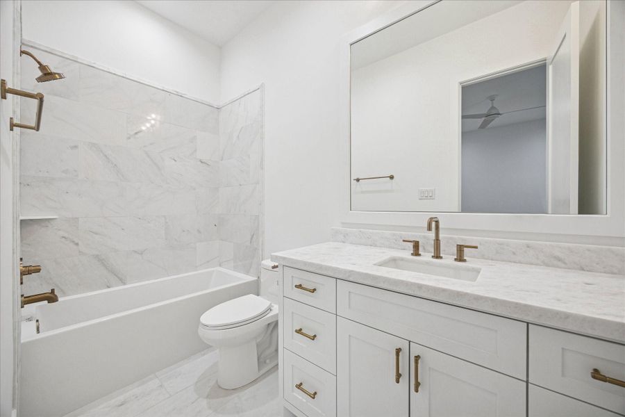 This bathroom offers a refined blend of modern comfort and classic elegance. The space features a full size soaking tub with marble pattern tile surround, paired with brushed brass fixtures for a warm elevated touch. The vanity includes shaker style cabinetry, a marble surface, and matching brass hardware with an under mount sink. Soft white walls and large scale tile flooring keep the room feeling open, bright, and calming. This bathroom offers a refined blend of modern comfort and classic elegance. The space features a full size soaking tub with marble pattern tile surround, paired with brushed brass fixtures for a warm elevated touch. The vanity includes shaker style cabinetry, a marble surface, and matching brass hardware with an under mount sink. Soft white walls and large scale tile flooring keep the room feeling open, bright, and calming.