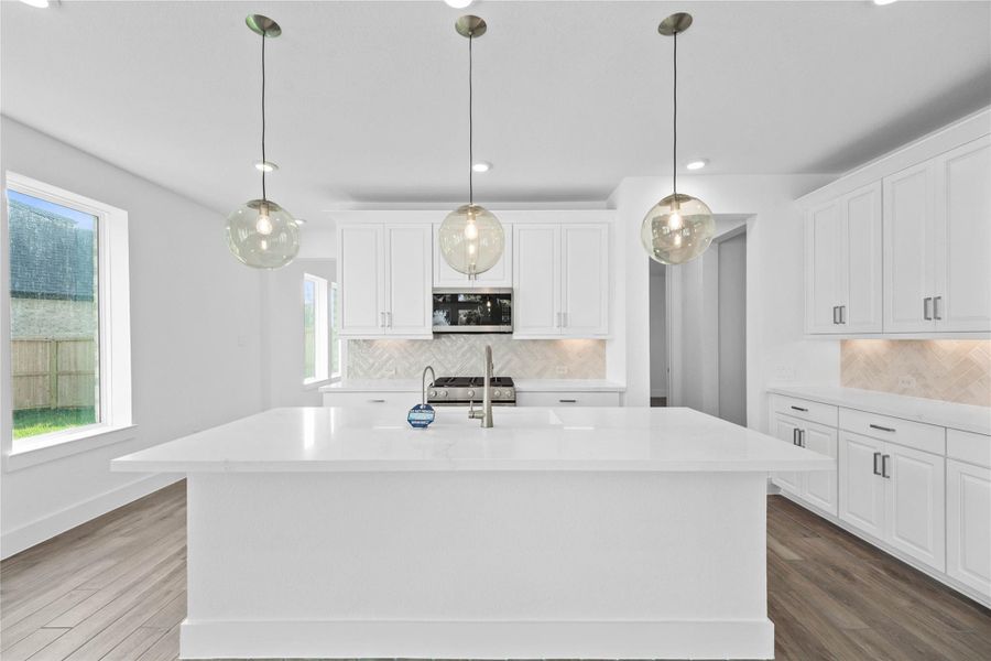 The stunning and generously sized center island features a breakfast bar, perfect for casual dining and entertaining. The island is beautifully designed with warm wood cabinetry, pristine white quartz countertop, and elegant pendant lights.