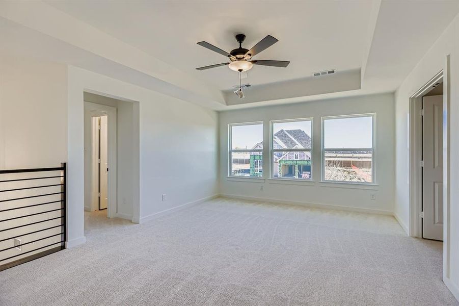Empty room featuring light carpet, a raised ceiling, and a ceiling fan Empty room featuring light carpet, a raised ceiling, and a ceiling fan