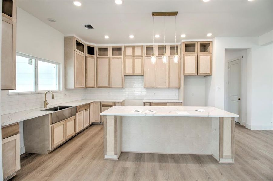 Kitchen with light brown cabinets, decorative backsplash, recessed lighting, light stone counters, and decorative light fixtures Kitchen with light brown cabinets, decorative backsplash, recessed lighting, light stone counters, and decorative light fixtures