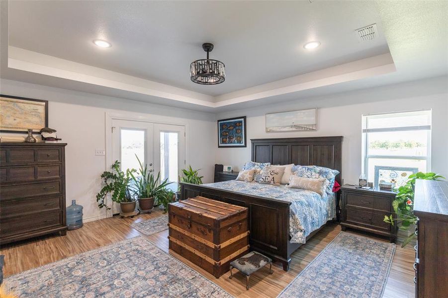Spacious room featuring wood-finish flooring and a tray ceiling with recessed lighting and a central chandelier Spacious room featuring wood-finish flooring and a tray ceiling with recessed lighting and a central chandelier