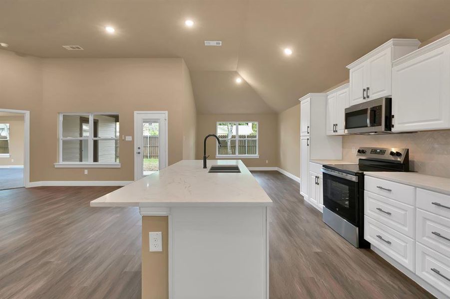 Kitchen featuring dark wood-style flooring, a sink, an island with sink, baseboards, and appliances with stainless steel finishes Kitchen featuring dark wood-style flooring, a sink, an island with sink, baseboards, and appliances with stainless steel finishes