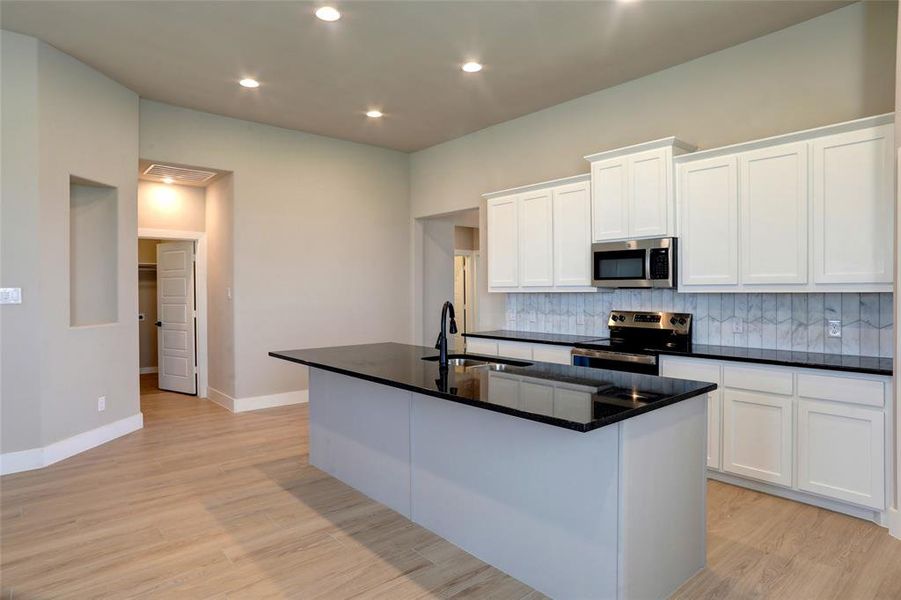 Kitchen featuring white cabinetry, a center island with sink, appliances with stainless steel finishes, dark stone countertops, and light wood-style flooring Kitchen featuring white cabinetry, a center island with sink, appliances with stainless steel finishes, dark stone countertops, and light wood-style flooring