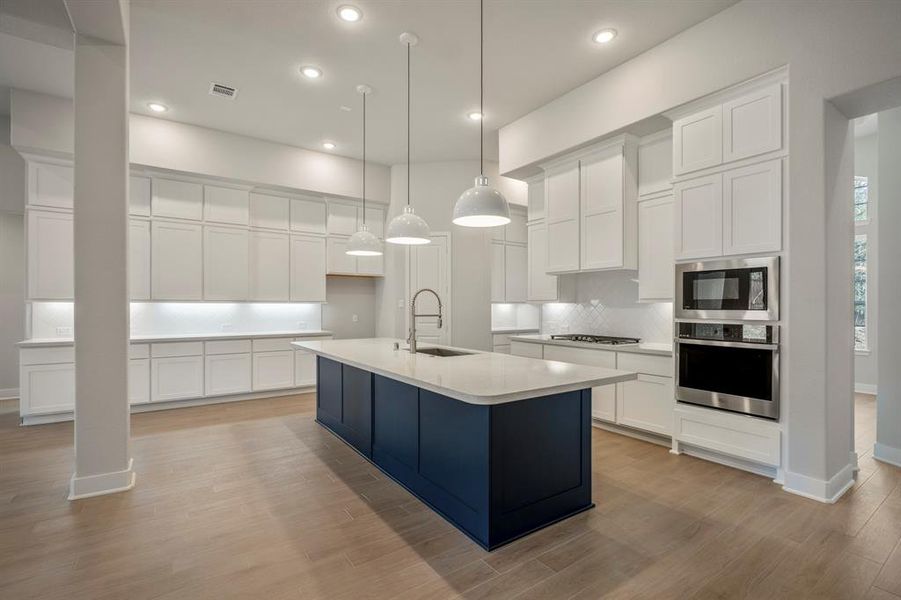 This kitchen's stunning open-plan design, featuring a chic blue island for the perfect pop of color. Elegant pendant lighting shines on sleek countertops, while abundant Benedettini cabinetry offers endless storage.